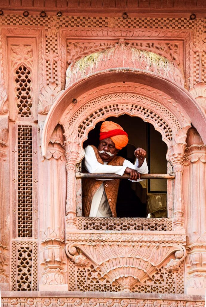 pexels-photo-19160094 A senior Indian man in a turban leans from an ornate window of a traditional building.