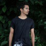 A young man poses casually outdoors against lush greenery in Bengaluru, India.